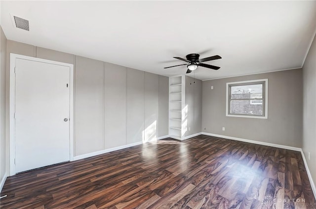 spare room featuring built in features, dark wood-style floors, a ceiling fan, visible vents, and baseboards