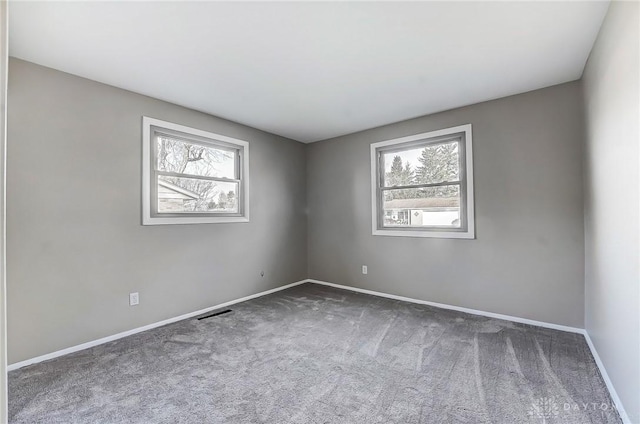 spare room featuring a wealth of natural light, visible vents, baseboards, and carpet flooring