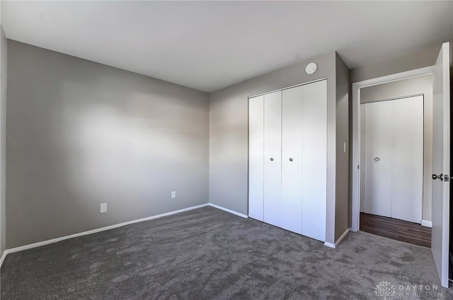 unfurnished bedroom featuring baseboards, a closet, and dark carpet