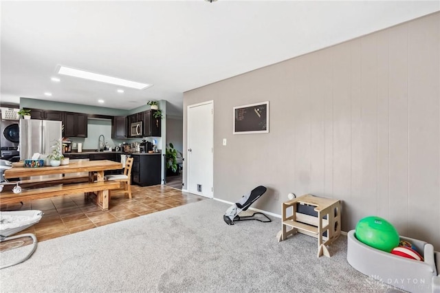 interior space featuring a sink, dark brown cabinetry, stacked washer and clothes dryer, appliances with stainless steel finishes, and light colored carpet