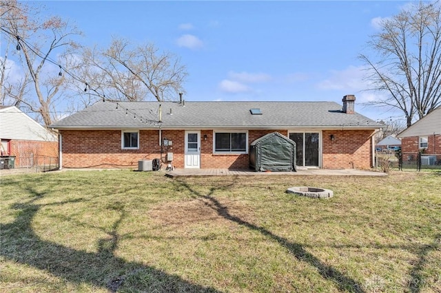 back of house featuring a yard, an outdoor fire pit, brick siding, and fence