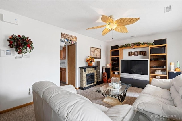 living area featuring visible vents, a ceiling fan, carpet, a stone fireplace, and baseboards