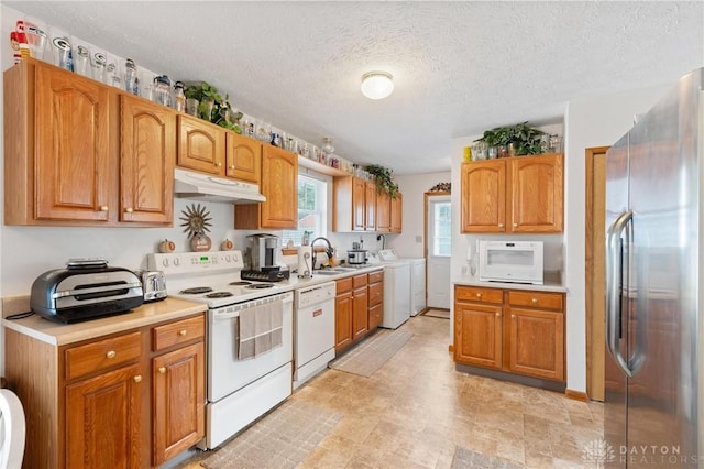 kitchen featuring white appliances, a sink, light countertops, under cabinet range hood, and independent washer and dryer