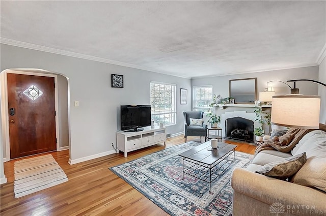 living room featuring a fireplace with flush hearth, arched walkways, crown molding, light wood finished floors, and baseboards