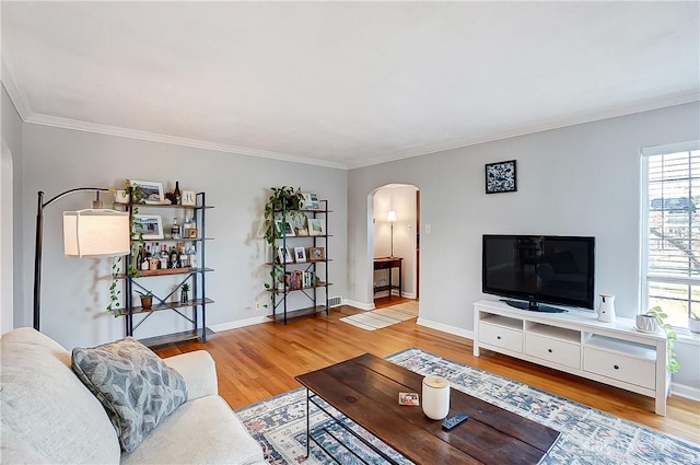 living area featuring arched walkways, ornamental molding, baseboards, and wood finished floors