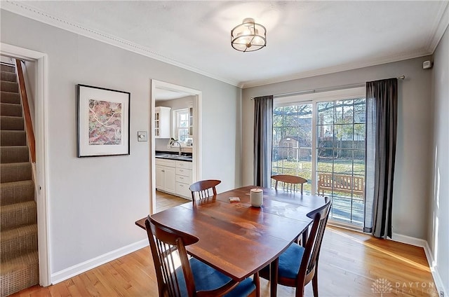 dining area featuring light wood-type flooring, baseboards, stairs, and crown molding