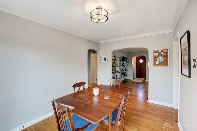 dining area with baseboards, arched walkways, ornamental molding, and light wood finished floors