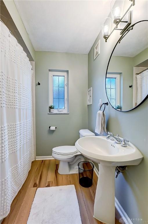 bathroom featuring a shower with curtain, wood finished floors, visible vents, baseboards, and toilet