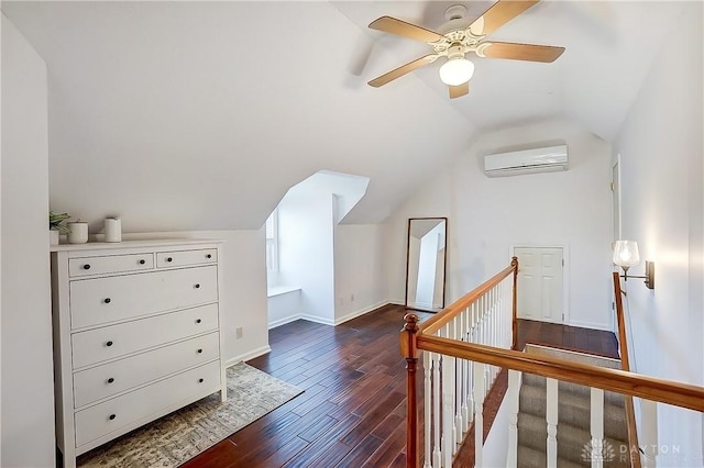 additional living space with a ceiling fan, baseboards, an AC wall unit, dark wood-type flooring, and vaulted ceiling