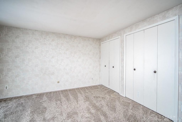 unfurnished bedroom featuring two closets and carpet