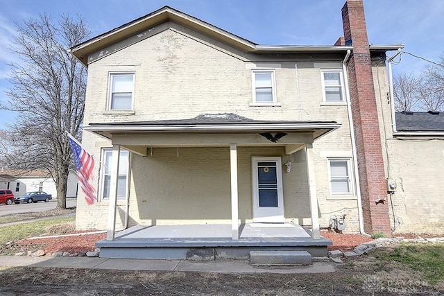 view of front of property with brick siding, covered porch, and a chimney