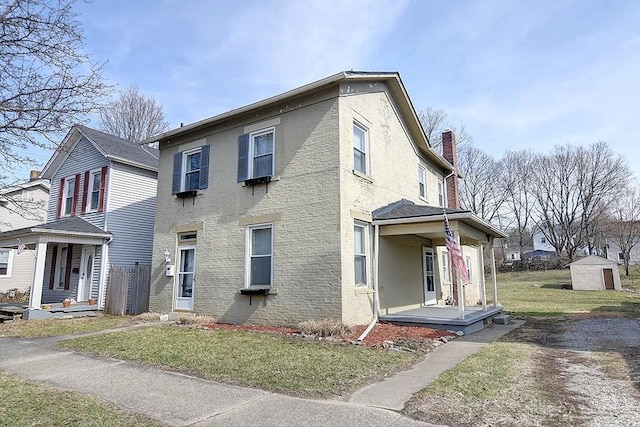 view of front of house with a front lawn, covered porch, brick siding, and a chimney