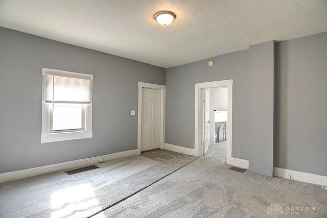 empty room with visible vents, carpet flooring, a textured ceiling, and baseboards