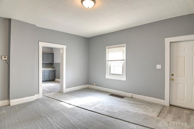 unfurnished room with visible vents, light colored carpet, a textured ceiling, and baseboards