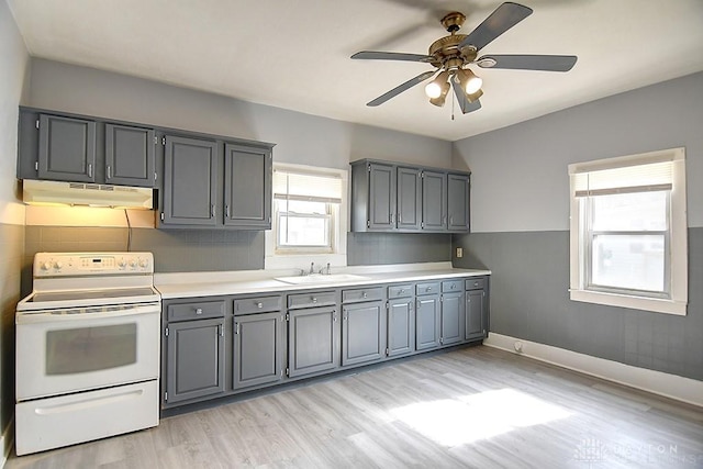 kitchen with gray cabinetry, electric stove, under cabinet range hood, a sink, and light wood-style floors