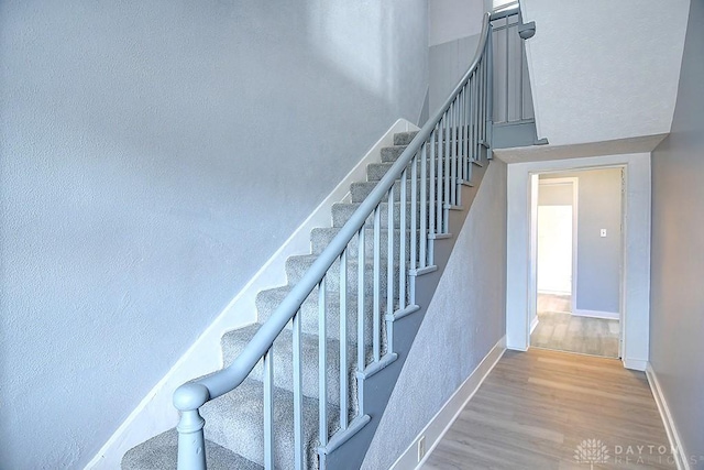 stairway featuring a high ceiling, baseboards, and wood finished floors