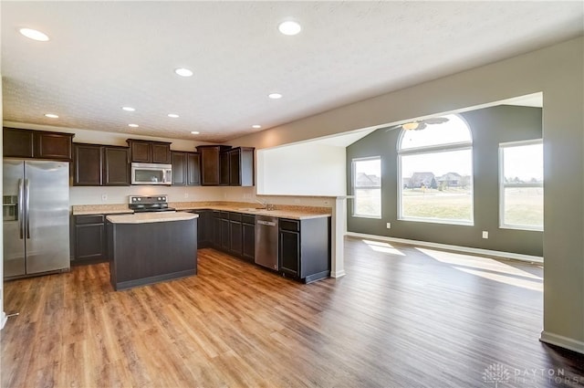 kitchen featuring dark brown cabinets, a center island, light countertops, appliances with stainless steel finishes, and wood finished floors