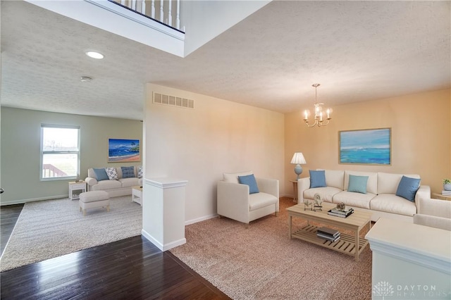 living area with a notable chandelier, wood finished floors, visible vents, and a textured ceiling