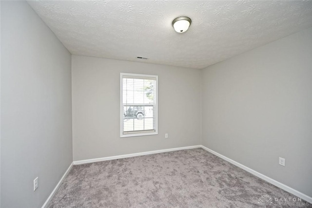 carpeted spare room featuring visible vents, baseboards, and a textured ceiling