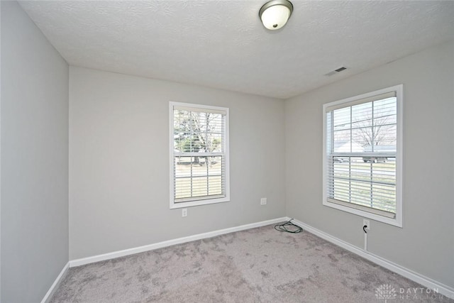 carpeted spare room featuring visible vents, baseboards, and a textured ceiling