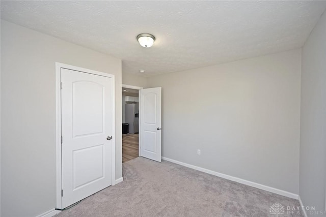 unfurnished room with light colored carpet, a textured ceiling, and baseboards