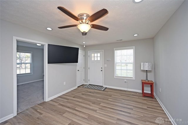 foyer featuring baseboards, a healthy amount of sunlight, a ceiling fan, and light wood finished floors