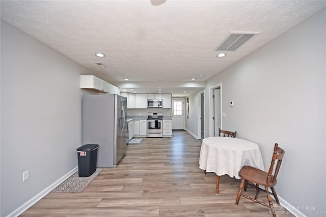 interior space featuring visible vents, baseboards, recessed lighting, light wood-style flooring, and a textured ceiling