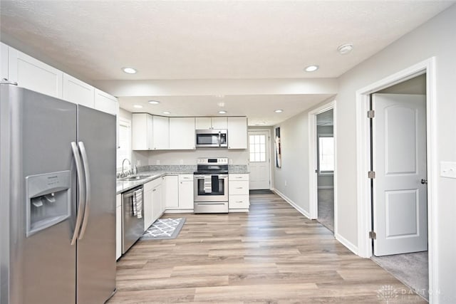 kitchen with light wood-style flooring, appliances with stainless steel finishes, white cabinetry, and a sink