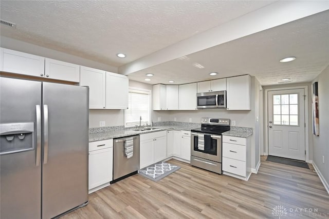 kitchen with a sink, stainless steel appliances, light wood-style floors, white cabinets, and light stone countertops