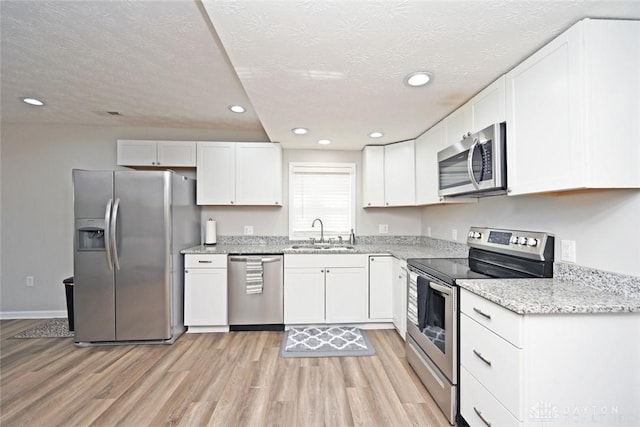 kitchen featuring a sink, light wood-style floors, appliances with stainless steel finishes, and white cabinets