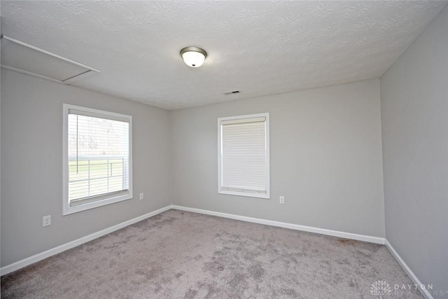 spare room featuring visible vents, baseboards, a textured ceiling, and carpet flooring