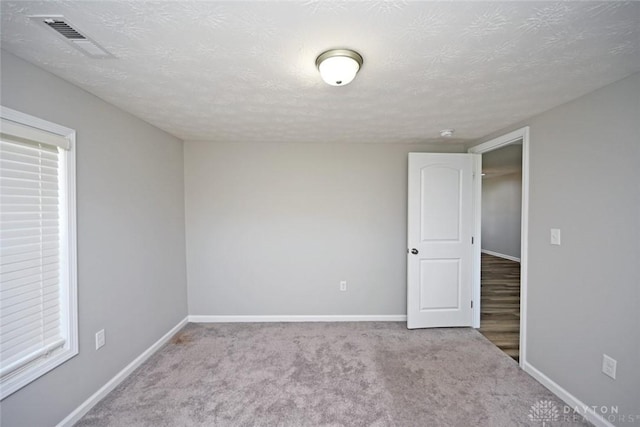 unfurnished room with visible vents, baseboards, a textured ceiling, and carpet flooring