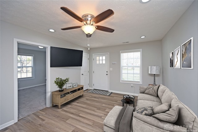 living area with a wealth of natural light, light wood finished floors, a textured ceiling, and ceiling fan