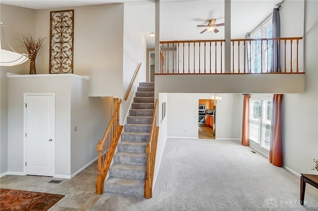 staircase featuring visible vents, ceiling fan with notable chandelier, a high ceiling, carpet flooring, and baseboards