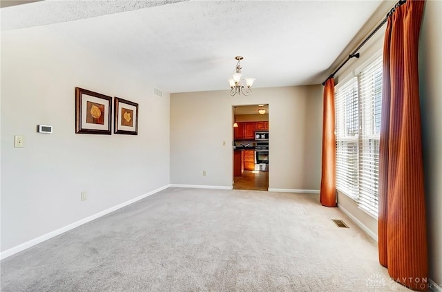 empty room featuring a notable chandelier, light colored carpet, visible vents, and baseboards