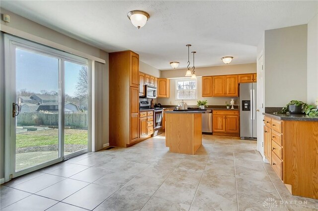 kitchen with dark countertops, a kitchen island, pendant lighting, brown cabinets, and stainless steel appliances