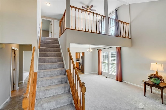 stairway featuring baseboards, carpet floors, a towering ceiling, and ceiling fan with notable chandelier