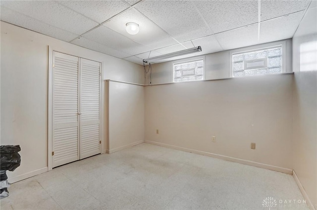 below grade area with a wealth of natural light, a paneled ceiling, baseboards, and tile patterned floors