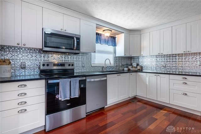 kitchen featuring a sink, tasteful backsplash, dark countertops, dark wood finished floors, and stainless steel appliances