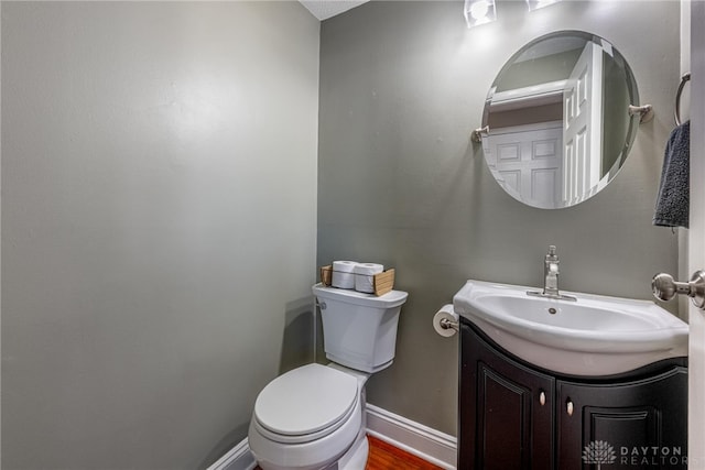 half bathroom featuring toilet, vanity, and baseboards