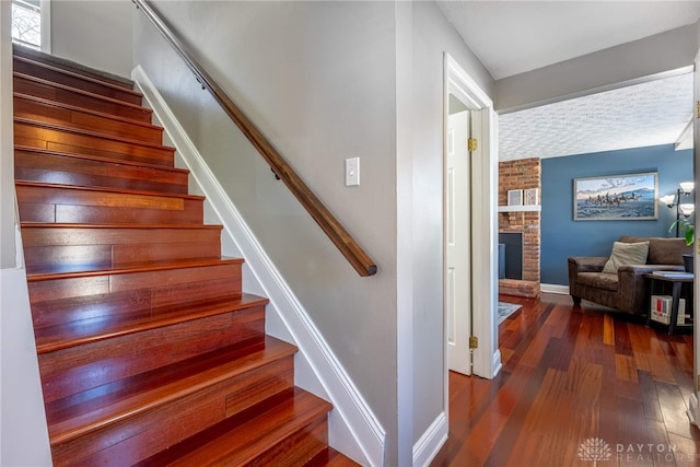 stairs featuring baseboards, a brick fireplace, and hardwood / wood-style flooring