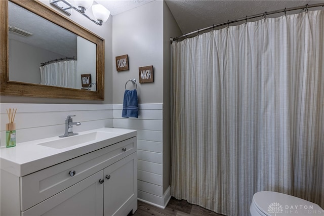 bathroom with visible vents, toilet, vanity, wood finished floors, and a textured ceiling