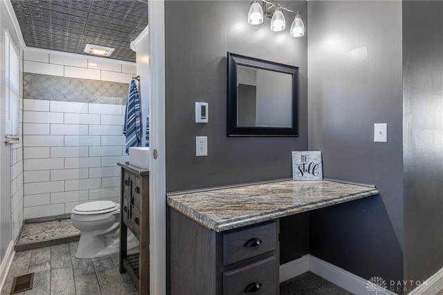 full bathroom featuring vanity, wood finished floors, visible vents, a tile shower, and toilet