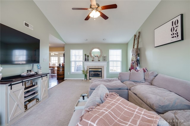 living area featuring visible vents, a tile fireplace, ceiling fan, vaulted ceiling, and light colored carpet