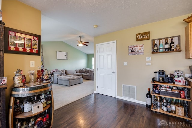 living area with a ceiling fan, visible vents, baseboards, dark wood finished floors, and vaulted ceiling