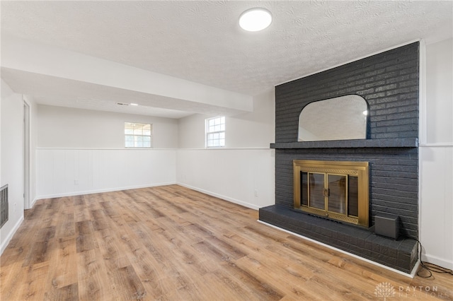 unfurnished living room featuring a wainscoted wall, a textured ceiling, wood finished floors, and a fireplace