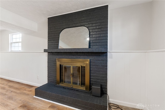 interior details featuring a brick fireplace, wood finished floors, a wainscoted wall, and a textured ceiling