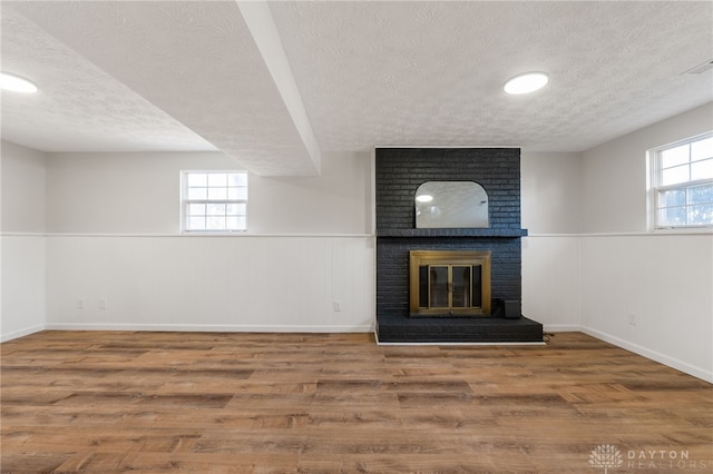 unfurnished living room featuring a wealth of natural light, a wainscoted wall, wood finished floors, and a fireplace