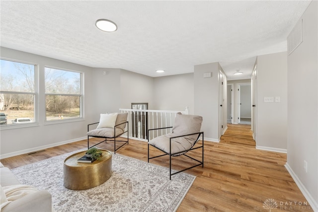 living area with light wood-type flooring, visible vents, an upstairs landing, a textured ceiling, and baseboards