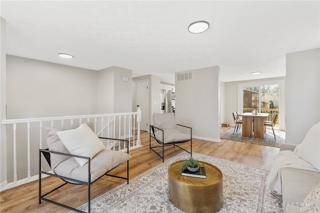 living area featuring an upstairs landing, visible vents, baseboards, and wood finished floors